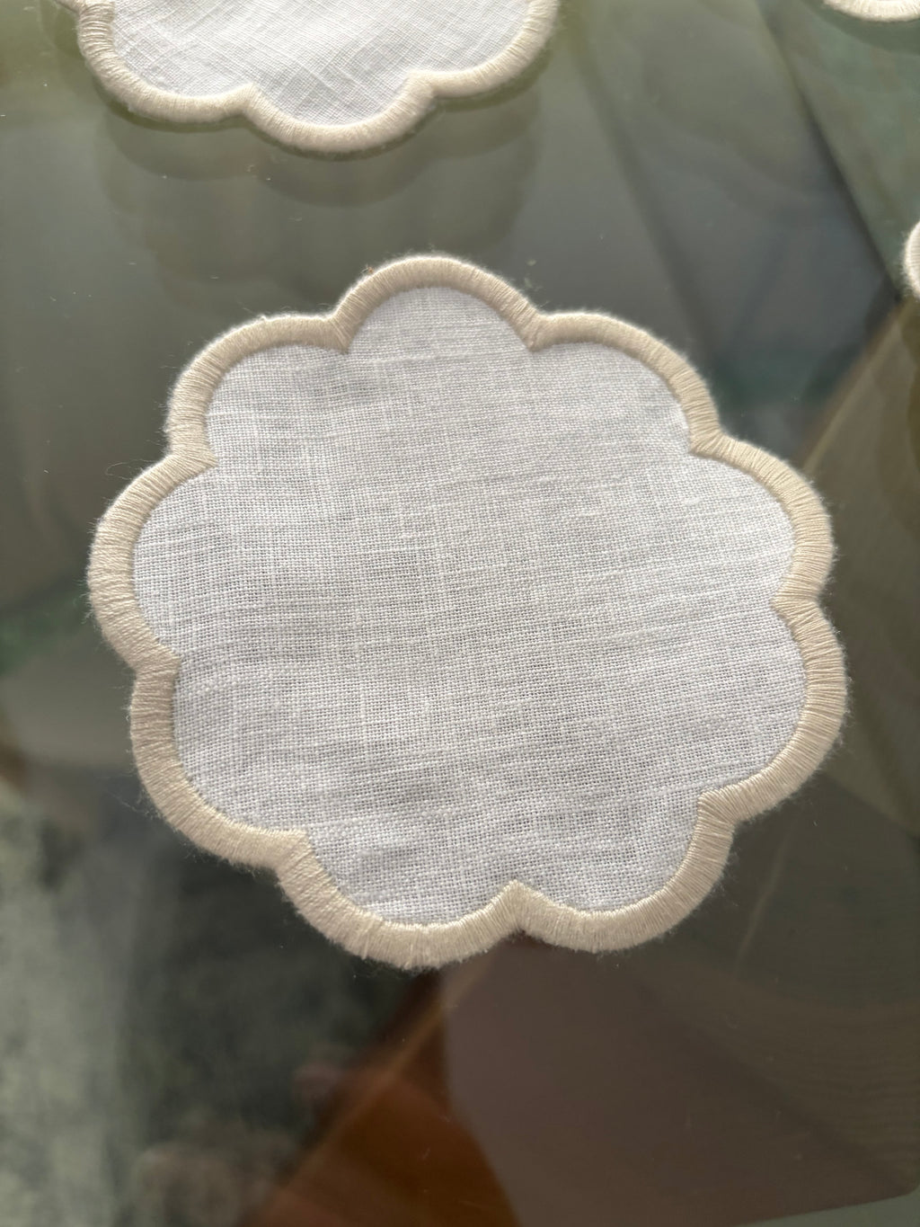Close-up of the sand embroidered scallop on a white linen coaster