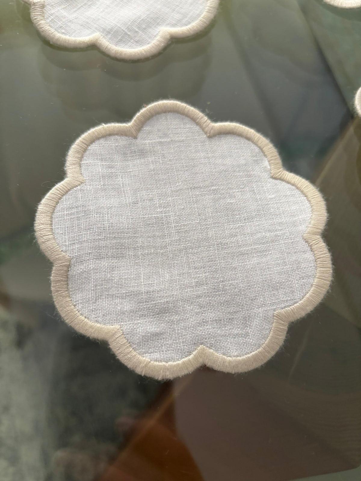Close-up of the sand embroidered scallop on a white linen coaster